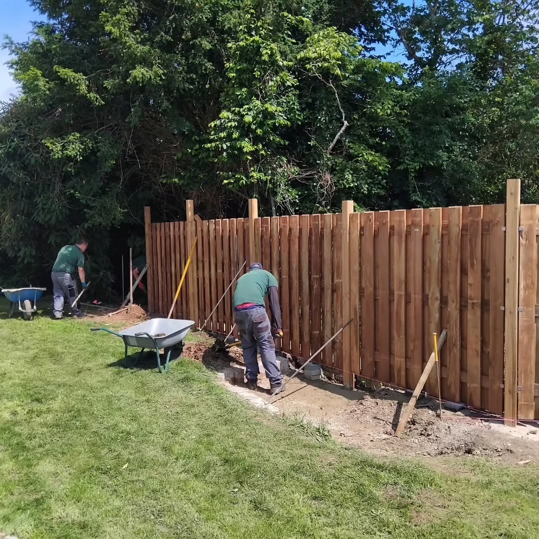 #Dourdan91 Deux ouvriers construisent une clôture en bois dans un jardin.